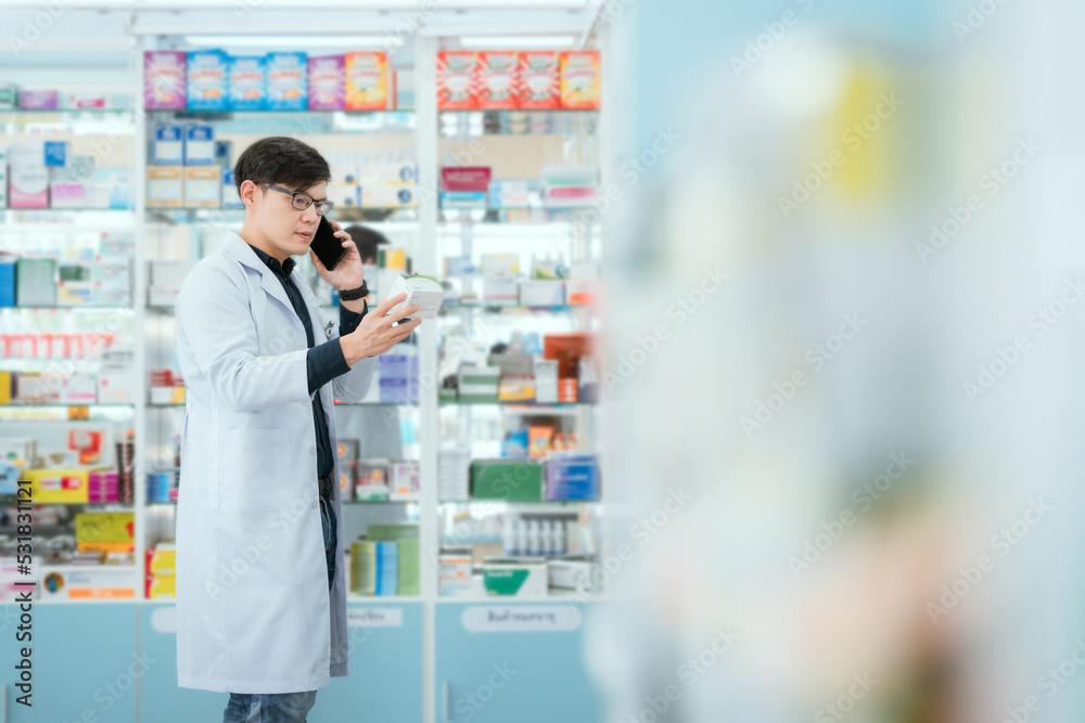 A male pharmacist checks drug stocks in a community pharmacy. use the phone to talk