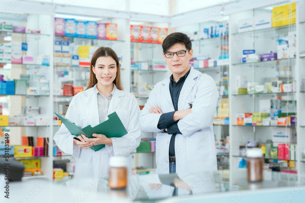 Male and female doctor-pharmacists look at the camera with smiles in a community pharmacy.