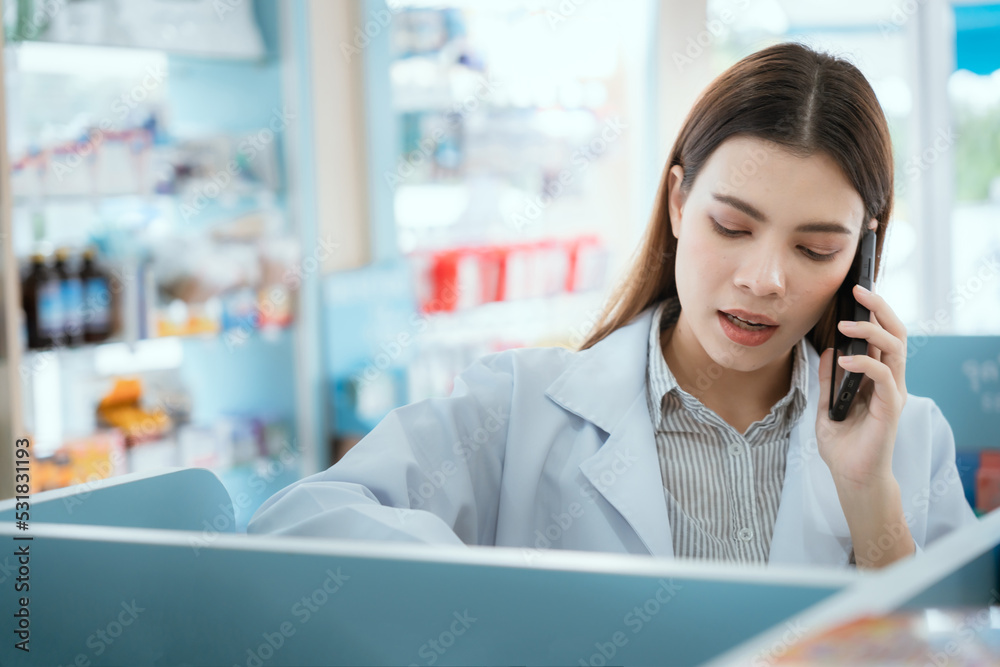 © 2B - A female pharmacist checks drug stocks in a community pharmacy. use the phone to talk