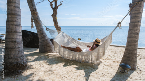 Couple of men and women watching the sunrise in a hammock on a tropical beach in Hua Hin Thailand. Asian women and European men in a hammock on the beach of Huahin Thailand photo