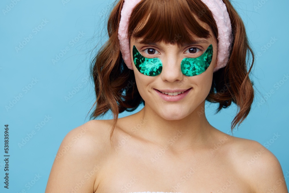 Naklejka premium a sweet, pleasant woman stands on a blue background with shiny blue patches on her eyes and a soft pink rim on her head, smiling happily while looking at the camera