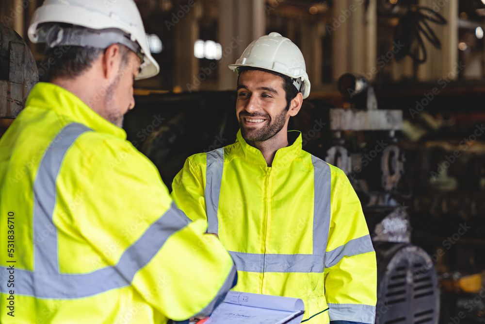 Caucasian factory engineer talking and shaking hands on business cooperation agreement. Successful hand shaking after good deal, workers handshaking each other at heavy industrial production line.