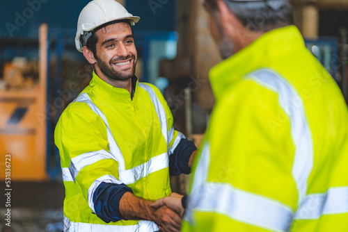 Caucasian factory engineer talking and shaking hands on business cooperation agreement. Successful hand shaking after good deal, workers handshaking each other at heavy industrial production line. photo