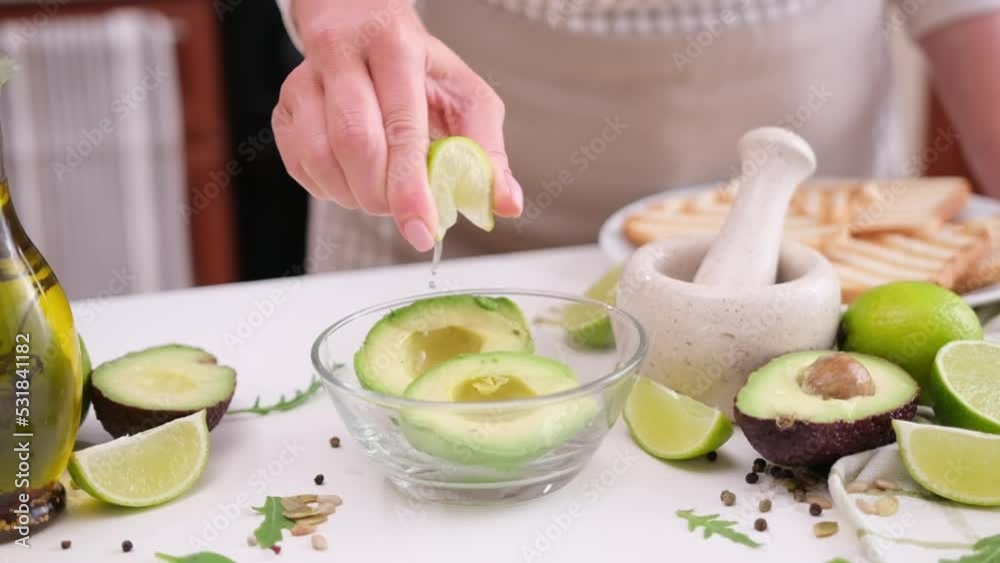 Woman squeezing fresh lime juice onto halved avocado at domestic kitchen Woman squeezing fresh lime juice onto halved avocado at domestic kitchen
