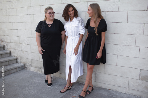 Tree friends, plus size woman and two strong girls walking in the streeet of the city against the urban whit wall. Female people dressed white and black dress photo