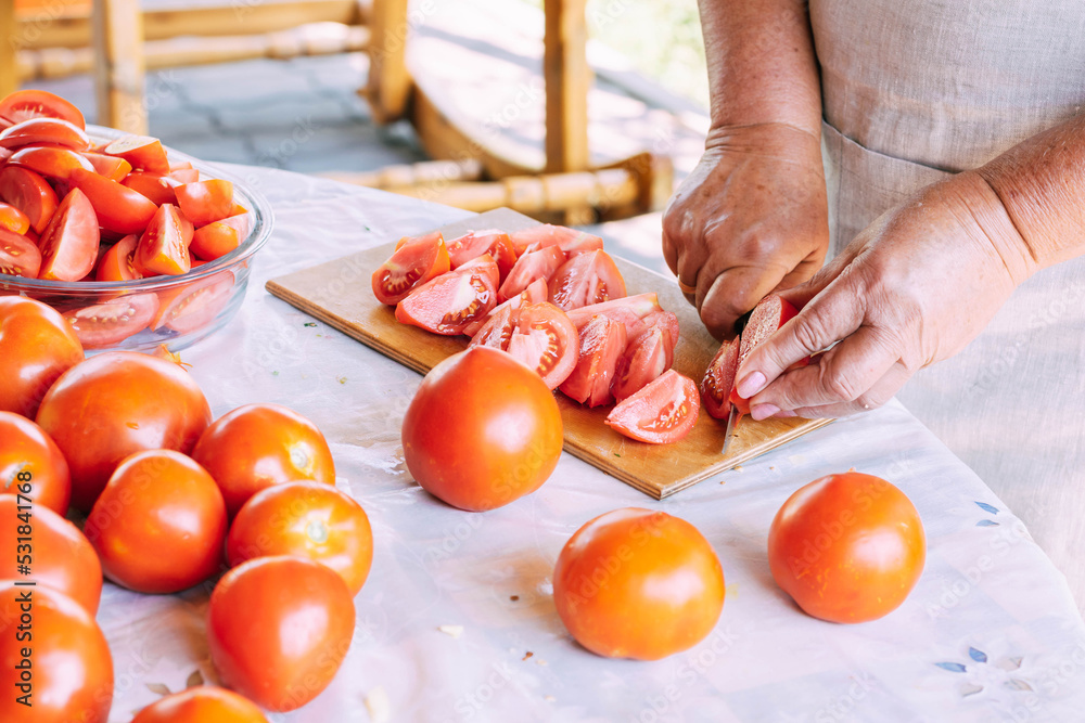 An elderly woman cuts fresh red tomatoes for salad, soup or sauce, farm organic vegetables