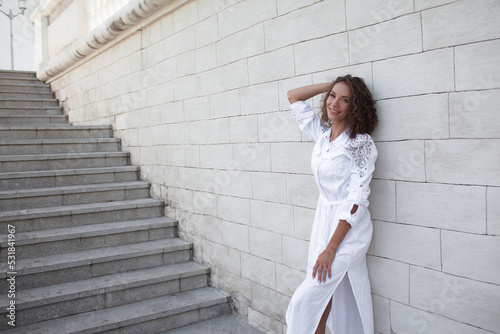 Beautiful curly woman walking in the street . Girl dressed white maxy dress and posing against street wall © Вероника Зеленина