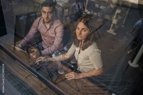 Shot from outdoors of two people in coffee bar looking through window.