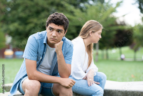 Pensive and sad hispanic boy thinking on couple relationship sitting back to back with girlfriend outdoors in a park © Egoitz