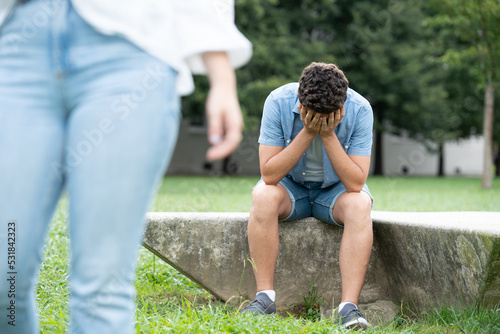 Sad boy sitting outdoors in a park and crying alone after breakup.