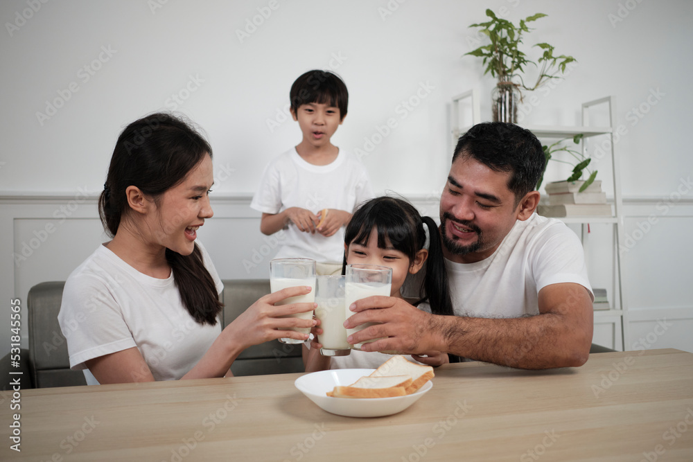 A Healthy Asian Thai family, little children, and young parents drink fresh white milk in glass and bread joy together at a dining table in morning, wellness nutrition home breakfast meal lifestyle. A Healthy Asian Thai family, little children, and young parents drink fresh white milk in glass and bread joy together at a dining table in morning, wellness nutrition home breakfast meal lifestyle.