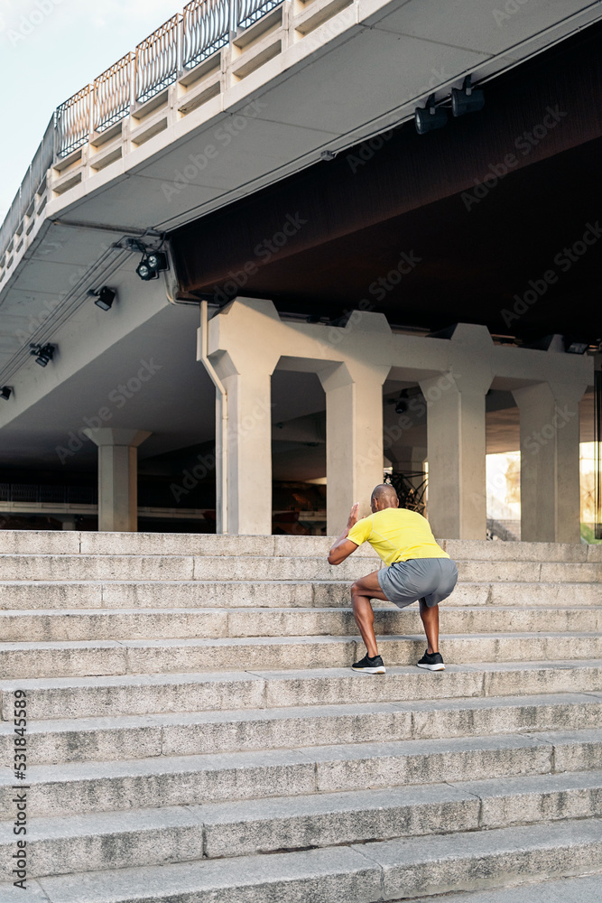 Unrecognizable adult man doing squats exercises on stairs outdoor