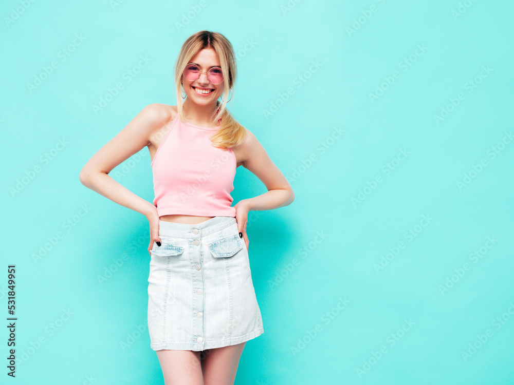 Young beautiful smiling blond female in trendy summer jeans skirt clothes. carefree woman posing near blue wall in studio. Positive model having fun indoors. Cheerful and happy Young beautiful smiling blond female in trendy summer jeans skirt clothes. carefree woman posing near blue wall in studio. Positive model having fun indoors. Cheerful and happy