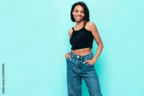 Portrait of young beautiful black woman. Smiling model dressed in summer jeans clothes. carefree female posing near blue wall in studio. Tanned and cheerful