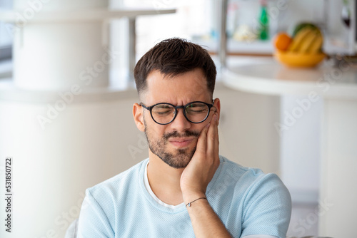 Depressed ill man having toothache and touching cheek. Young man suffering from tooth pain, caries. Male suffering from toothache, closeup. Portrait of casual man toothache with painful expression photo