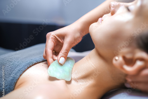 Woman having an gua sha facial massage with natural jade stone massager in the salon photo