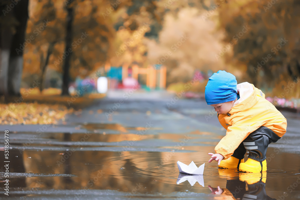paper boat puddle game, boy seasonal autumn look raincoat, yellow rubber boots, outdoor game paper boat puddle game, boy seasonal autumn look raincoat, yellow rubber boots, outdoor game
