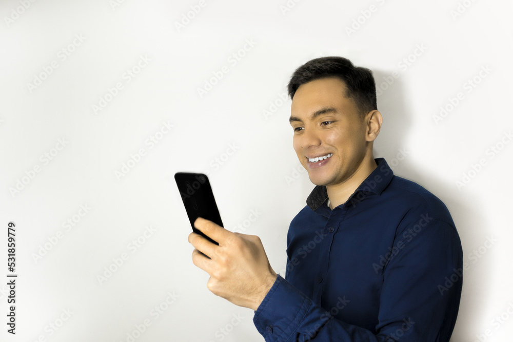 Hombre latino sonriente usando camisa azul, mirando teléfono. Hombre latino sonriente usando camisa azul, mirando teléfono.