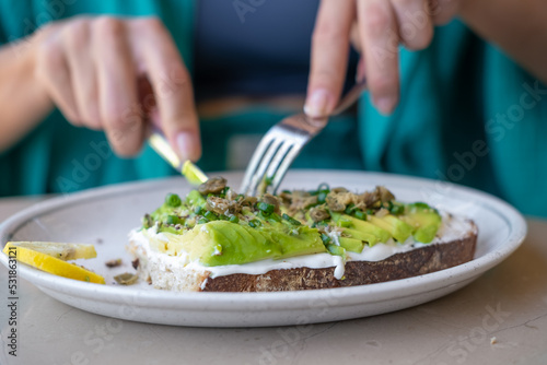 Woman eating avocado toast in cafe. Female hand cutting tasty sandwich or bruschetta.
