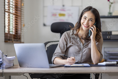 Asian indian woman entrepreneur busy with her work in the office. Young Asian woman talking over smartphone or cellphone while working on computer in workplace an home office.