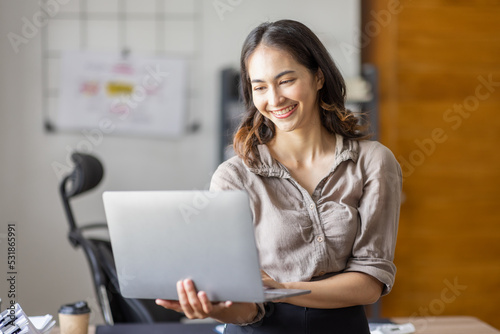 Smiling Happy indian Asian businessman standing and  holding a laptop in workplace an home office. © David