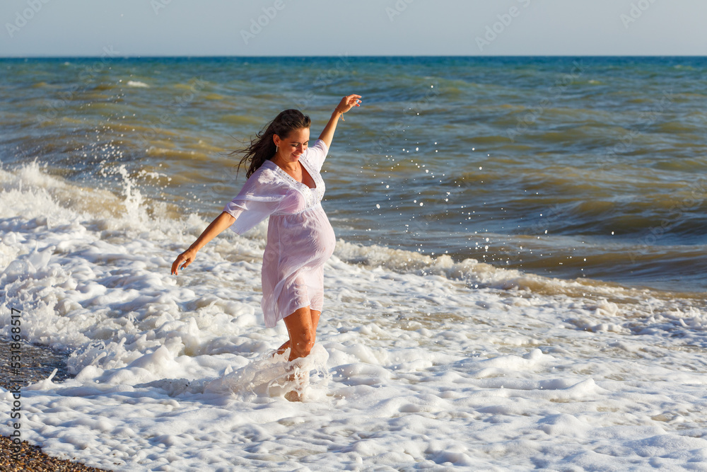 Pregnant woman is jumping on beach. Cheerful pregnant woman runs on