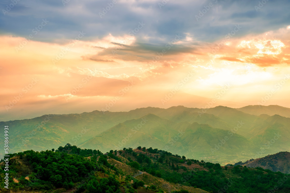 beautiful highland landscape with amazing view from a top with golden grass and green bushes to a canyon with majectic mountains and scenic cloudy sunset on background