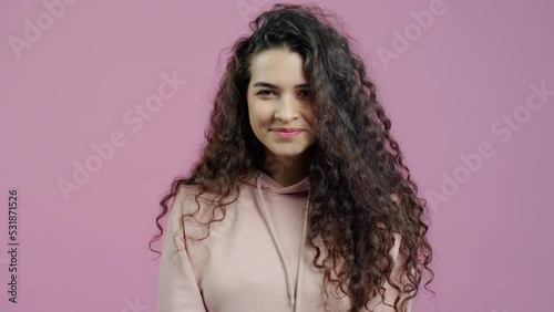 Portrait of cute young woman making heart hand gesture and winking smiling standing on pink background. Romantic youth and love concept.