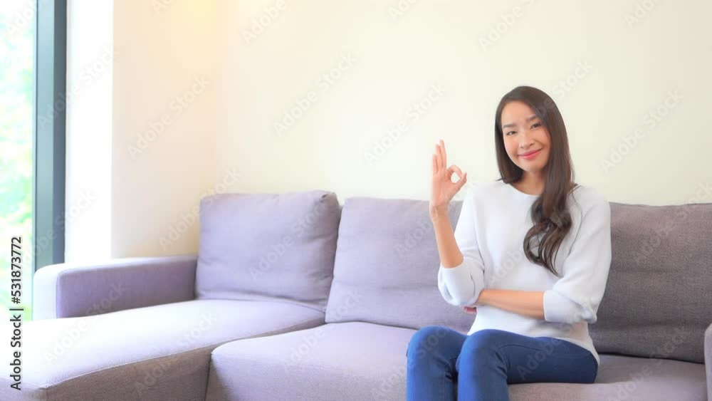 A pretty young woman sitting on a couch dressed in jeans and a sweater flashes the ok sign. A pretty young woman sitting on a couch dressed in jeans and a sweater flashes the ok sign.