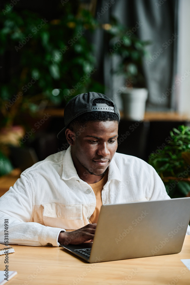 Young African American businessman concentrating on work with online data while sitting in front of laptop and preparing presentation