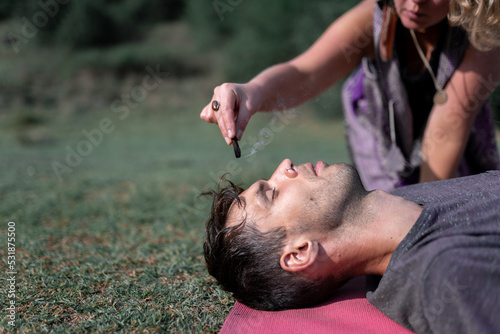 Crop woman with incense stick practicing hypnosis with calm man lying with closed eyes