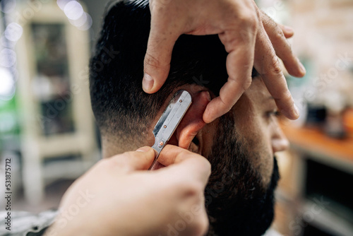 Crop barber cutting hair of client with razor photo