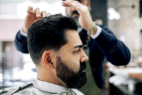 Crop barber brushing hair of client in salon