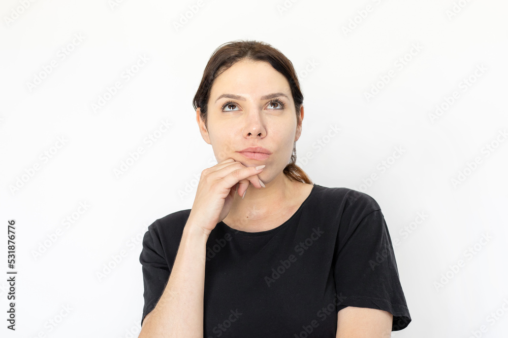 Portrait of thinking young woman. Female model in black t-shirt with dark hair looking up, touching chin. Portrait, studio shot, emotion concept Portrait of thinking young woman. Female model in black t-shirt with dark hair looking up, touching chin. Portrait, studio shot, emotion concept