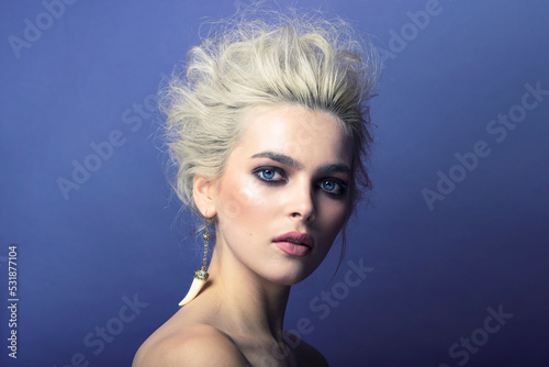 Profile portrait of a girl with make-up and hairdo, with bare shoulders, wear an earring, isolated blue background.