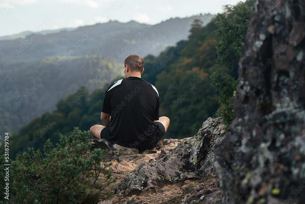 a strong athletic man sits on a high mountain rise with his back to us, rests and enjoys the view of nature during a hiking trip a strong athletic man sits on a high mountain rise with his back to us, rests and enjoys the view of nature during a hiking trip