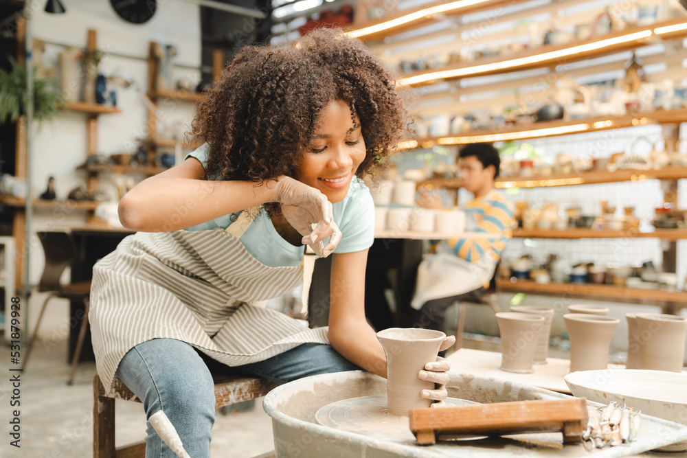 Creative afro American young woman artist molding clay on pottery wheel, Workshop in ceramic studio, clay making of a ceramic pot on the pottery wheel, hobby and leisure with pleasure concept Creative afro American young woman artist molding clay on pottery wheel, Workshop in ceramic studio, clay making of a ceramic pot on the pottery wheel, hobby and leisure with pleasure concept