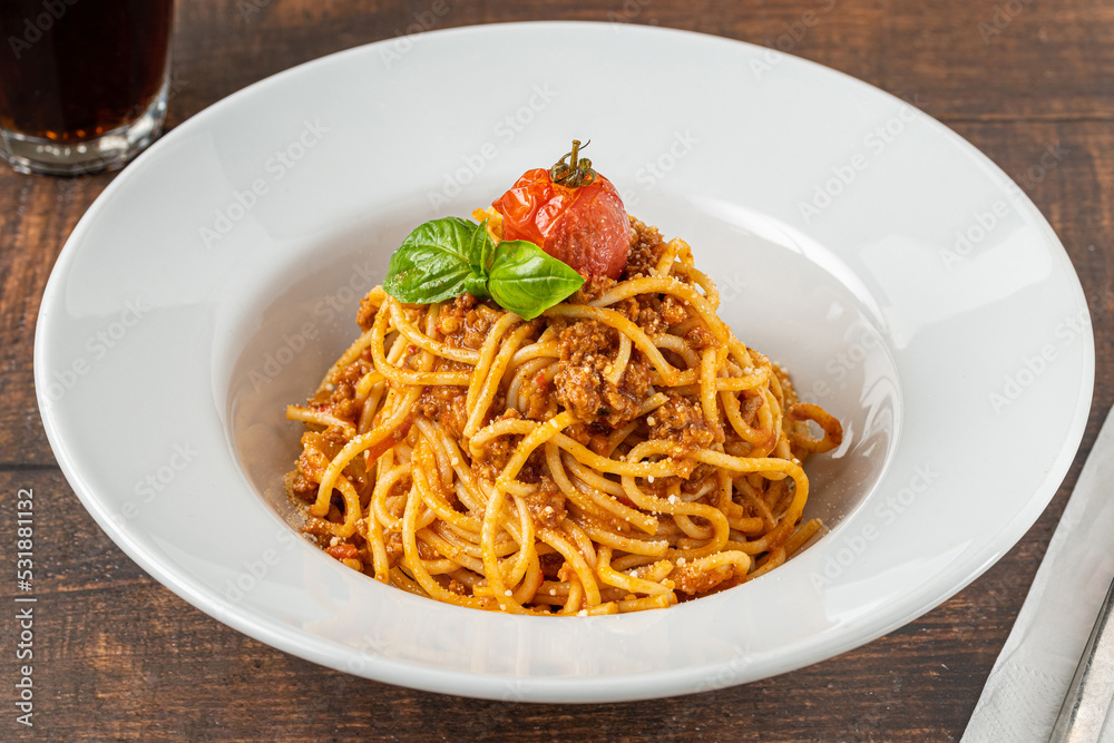 Spaghetti with bolognese sauce on white porcelain plate on wooden table