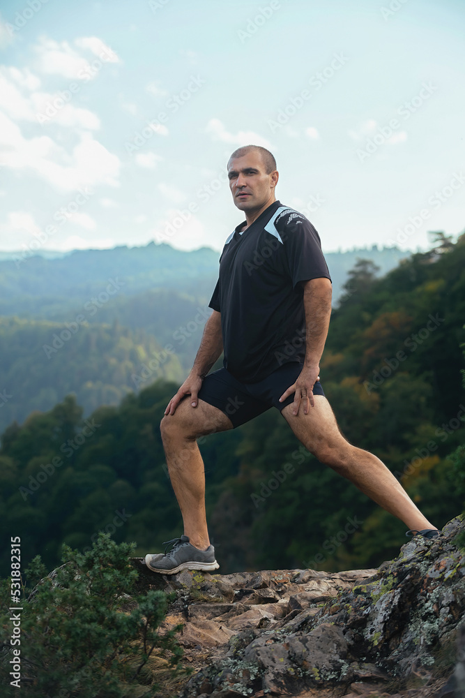 sports man doing stretching and exercising on the slope of a high mountain, the man creates a difficult workout in extreme conditions, trains his coordination and endurance sports man doing stretching and exercising on the slope of a high mountain, the man creates a difficult workout in extreme conditions, trains his coordination and endurance