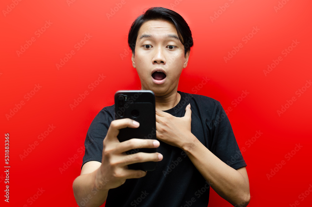 Shocked face of Asian man in black shirt on red background. man surprised receiving good news from the phone. Shocked face of Asian man in black shirt on red background. man surprised receiving good news from the phone.