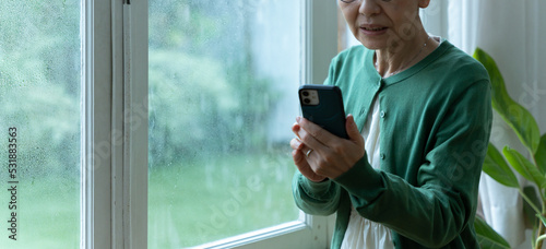 Foto 災害時にスマホで連絡をするシニア女性（避難警報・台風）