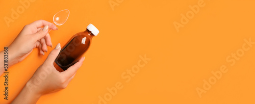 Female hands holding bottle of cough syrup and spoon on orange background with space for text photo
