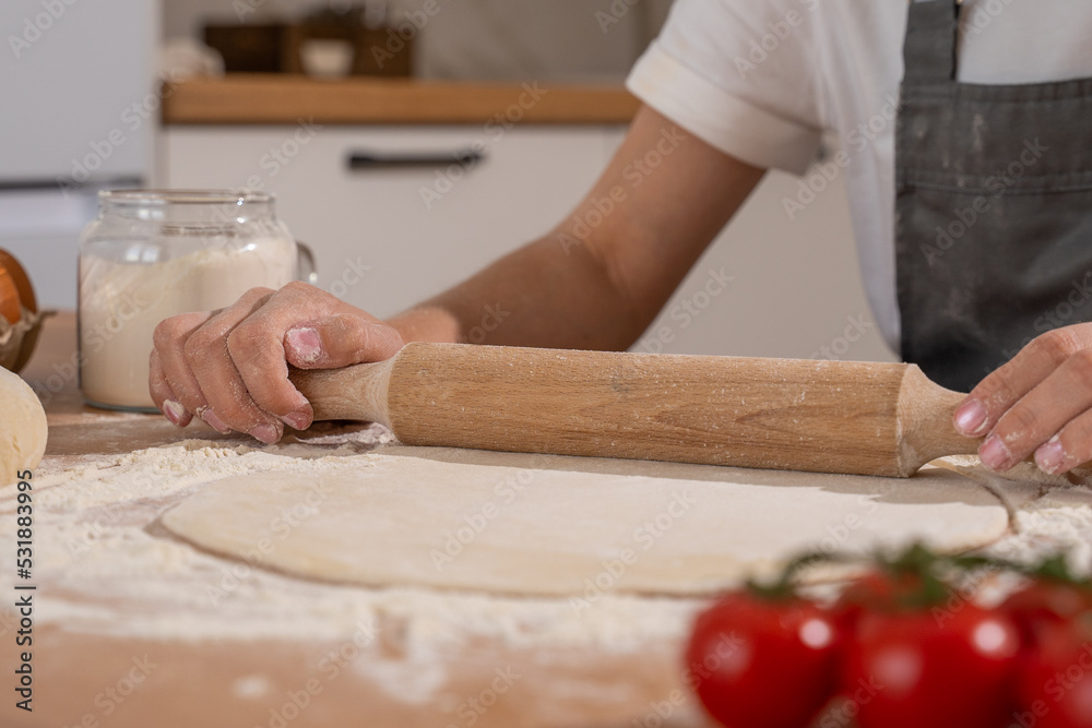 Hands of pastry woman rolling out dough with rolling pin on the table. 