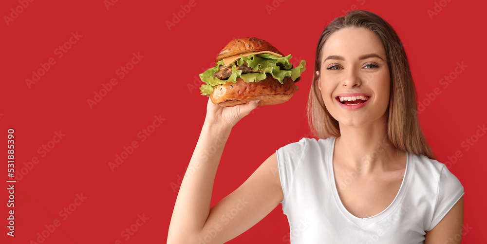 Beautiful happy young woman holding tasty burger on red background