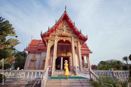 Travel by Asia . Young woman in hat and yellow dress walking near the Chalong buddhist temple on Phuket Island in Thailand.