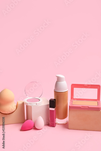 Makeup sponges with decorative cosmetics and blocks on pink background