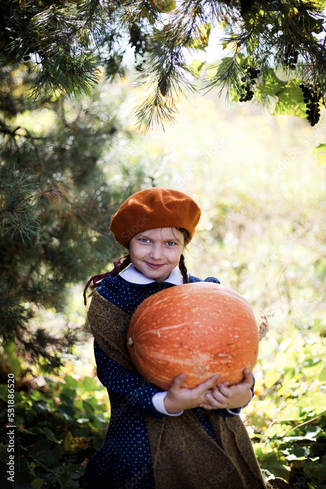 Dziewczynka w berecie i jesiennych barwach trzyma wielką dynię - obrazy, fototapety, plakaty 