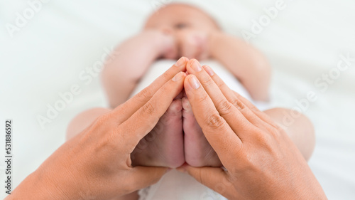 Mother is holding a foots of the newborn on white sheet background. Mom and baby