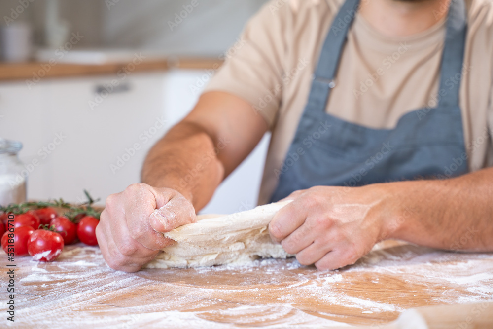 Baking concept. Unrecognizable male hands knead dough against the background of the kitchen. 