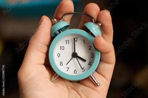 a small blue alarm clock showing 4 hours of time in your hand on a blurry background